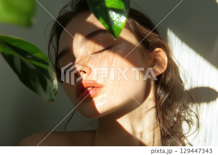 Young woman with olive complexion illuminated by soft sunlight on plain background 129447343
