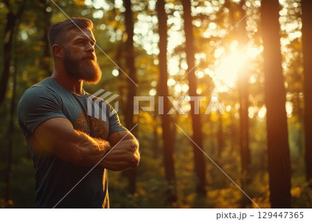 Man with rugged features stands confidently in serene forest bathed in warm sunlight 129447365