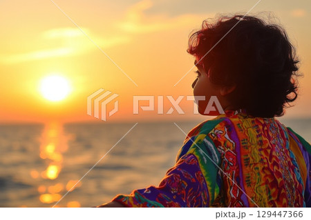 Child with curly black hair enjoys sunset at the beach wearing a colorful shirt 129447366