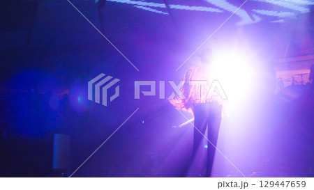 An unrecognized fashion model walks confidently on stage under bright lights, showcasing vibrant outfit and dynamic movement in an energetic atmosphere 129447659