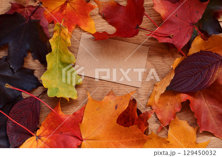 Autumn theme background with leaves over oak wood table with brown paper card 129450032