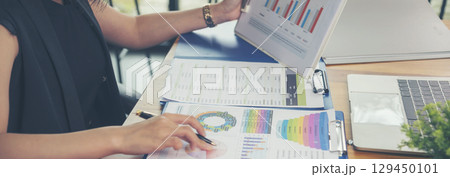 Asian Female freelance using laptop at home office desk. Woman reading financial graph chart Planning analyzing marketing data. Asian female people working office firm with business stuff, coffee cup 129450101