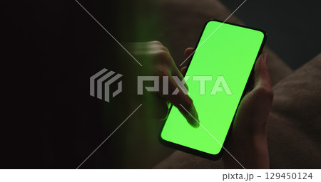 Young woman sitting on a couch and using smartphone with green screen 129450124