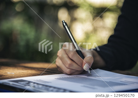 Woman hands writing empty notebook planing meeting agenda on wooden table. Close up women hands using pen drinking coffee cup planning office paper. Female hand holding pen note Personal Organizer 129450170