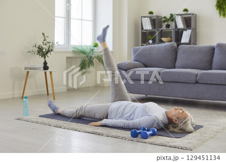 Sport exercises and healthy home workout of senior woman lying on yoga mat on floor with one leg up Sport exercises and healthy home workout of senior woman lying on yoga mat on floor with one leg up 129451134