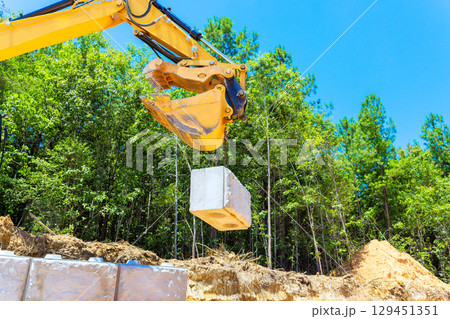 Excavator is lifting concrete block at construction site in wooded area under build retaining walls 129451351