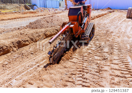 Construction crew utilizes trenching machine to create deep trench for utility lines at building site 129451387