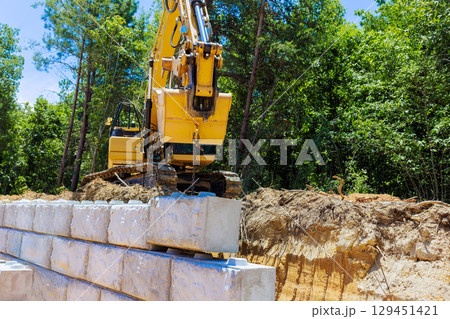 Heavy machinery is engaged in lifting concrete blocks at construction site build retaining walls 129451421