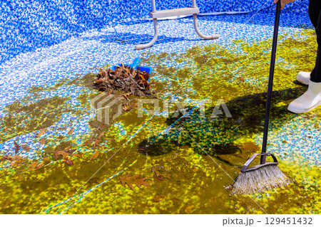 Worker cleans algae debris from bottom of swimming pool in private garden under works day Worker cleans algae debris from bottom of swimming pool in private garden under works day 129451432