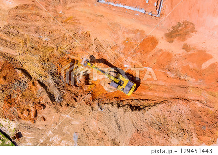 Excavator digs into soil, changing terrain for construction under works day 129451443