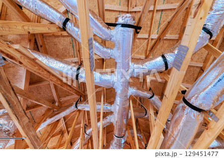 Ducts are placed among wooden beams in house being built, highlighting ventilation system setup. Ducts are placed among wooden beams in house being built, highlighting ventilation system setup. 129451477