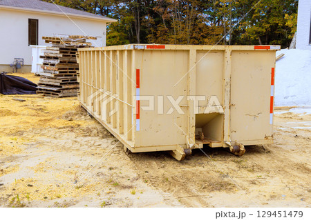 Large waste container sits on construction site surrounded by wooden pallets debris during works day hours. 129451479