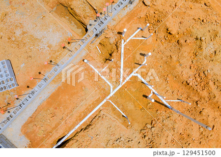Detailed view of construction site displaying intricate PVC piping plumbing installation configurations on dry terrain. 129451500