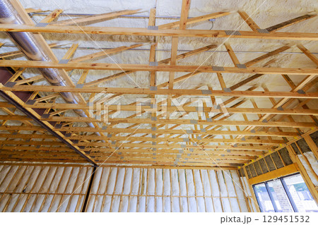 Wooden beams frame ceiling of an under construction room, installation insulation materials along walls. 129451532