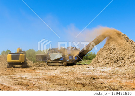 Large machine piles wood chips while another aids in land clearing dusty background. 129451610