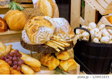Rustic bakery showcases an array of freshly baked bread, pastries, seasonal fruits under warm light. 129451633