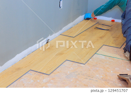 Carpenter installs wooden floor planks carefully along wall in residential space. 129451707