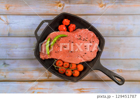 Raw beef cut sits in skillet surrounded by fresh tomatoes, green peppers, ingredients for meal. Raw beef cut sits in skillet surrounded by fresh tomatoes, green peppers, ingredients for meal. 129451787