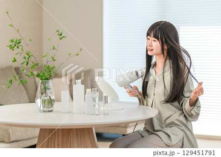 ヘアドライヤーでヘアブロー・髪の毛を乾かす女性（ヘアケア） 129451791