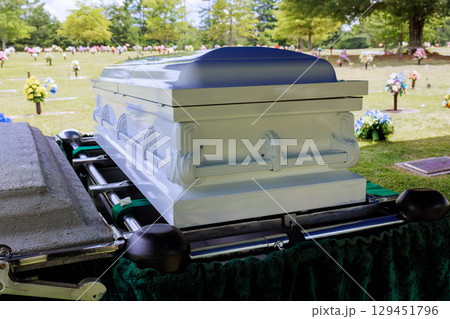 Casket is positioned at gravesite with colorful flowers greenery in peaceful cemetery during memorial service. 129451796