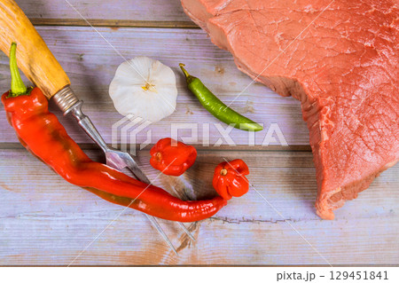 Slices of beef alongside vibrant peppers, garlic on rustic wood table, ready for culinary preparation. 129451841