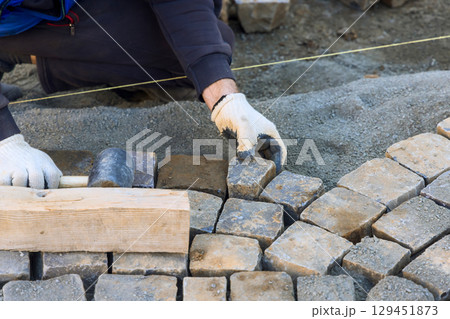 Skilled worker carefully positions stone bricks for pathway, ensuring they fit securely evenly on work day. 129451873