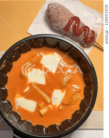 Chewy rose yeotteok coated in spicy pink sauce paired with a crispy corndog, blending sweet, savory, and spicy flavors. A trendy Korean street food duo perfect for food promotions. 129451939
