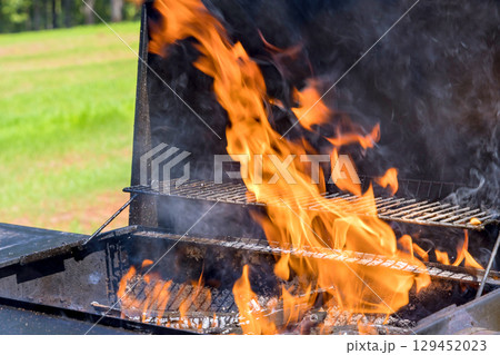 Barbecue grill releases flames smoke while cooking food during summer gathering in private backyard. Barbecue grill releases flames smoke while cooking food during summer gathering in private backyard. 129452023