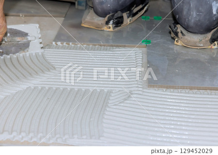 Construction workers apply adhesive on floor for tile installation in bright work area. Construction workers apply adhesive on floor for tile installation in bright work area. 129452029
