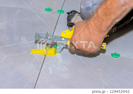 Carpenter carefully adjusts tiles using leveling tool for an even finish in home improvement project. 129452042