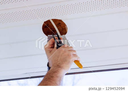 Electrical uses tools to install ceiling light fixture in home while natural light fills space. Electrical uses tools to install ceiling light fixture in home while natural light fills space. 129452094