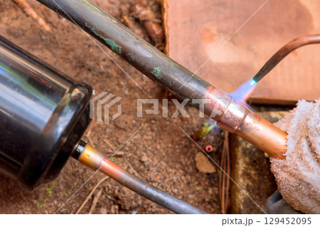Technician solders copper tubing while performing HVAC repairs in workshop repair work. Technician solders copper tubing while performing HVAC repairs in workshop repair work. 129452095