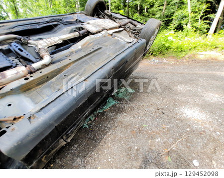 An overturned vehicle lies on its side on gravel road bordered by trees, indicating recent incident. 129452098