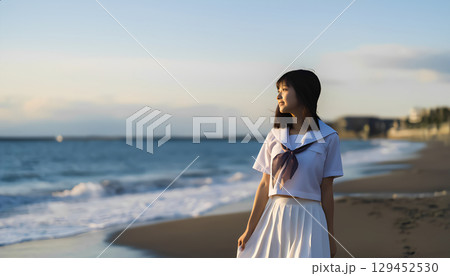 夕焼けの海岸を歩く女子高校生 129452530
