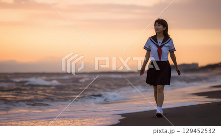 夕焼けの海岸を歩く女子高校生 129452532