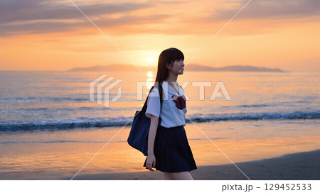 夕焼けの海岸を歩く女子高校生 129452533