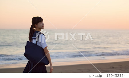 夕焼けの海岸を歩く女子高校生 129452534