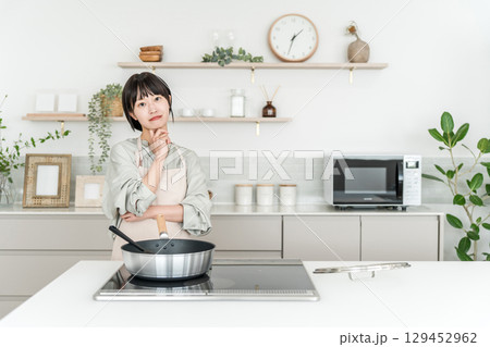 キッチンのIHコンロの前で考える,悩む迷いながら料理するエプロン姿の若いアジア人女性 キッチンのIHコンロの前で考える,悩む迷いながら料理するエプロン姿の若いアジア人女性 129452962