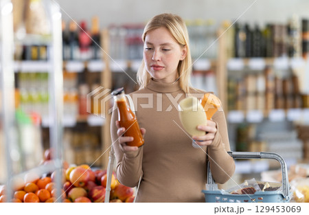 Girl buyer examine good, doubt and choose between varieties sauce in store Girl buyer examine good, doubt and choose between varieties sauce in store 129453069