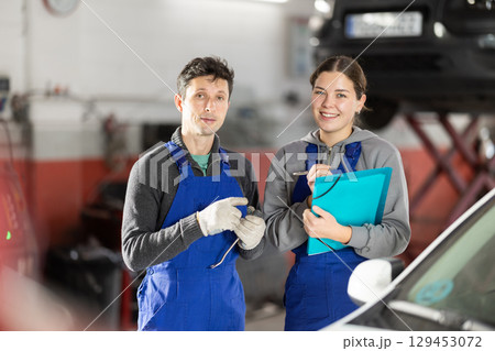 Car service manager discusses car repair problems with mechanic. He takes notes on paper 129453072
