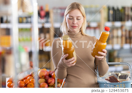 Young woman buyer chooses peach juice Young woman buyer chooses peach juice 129453075