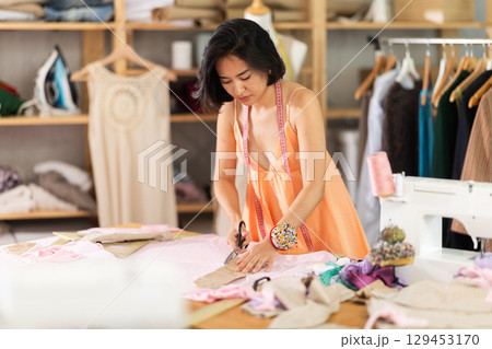 Woman seamstress cutting fabric in sewing workshop Woman seamstress cutting fabric in sewing workshop 129453170