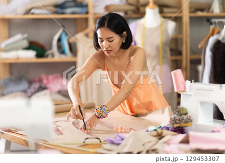 Woman seamstress drawing pattern on paper in workshop 129453307