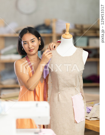 Woman seamstress adjusts clothes on mannequin 129453317