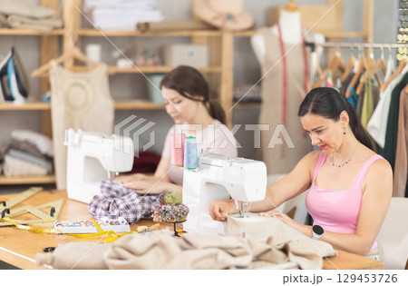 Two seamstresses working on sewing machines in sewing workshop Two seamstresses working on sewing machines in sewing workshop 129453726