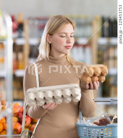 Young woman choosing eggs in grocery store 129453753