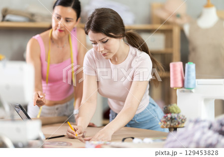 Using ruler and chalk, women tailor draws dress diagram scheme on paper Using ruler and chalk, women tailor draws dress diagram scheme on paper 129453828