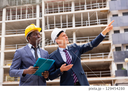 Young architect discussing a construction plan with a colleague points to something Young architect discussing a construction plan with a colleague points to something 129454280
