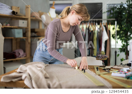 Young female dressmaker drawing on textile in sewing workshop Young female dressmaker drawing on textile in sewing workshop 129454435