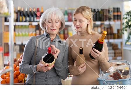 Shopping in produce supermarket - two female buyer makes choice bottle of wine Shopping in produce supermarket - two female buyer makes choice bottle of wine 129454494